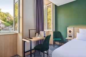 a hotel room with a bed and a desk and a bed and window at Le Grand Hôtel, The Originals Relais in Évaux-les-Bains