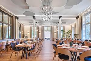 een restaurant met houten tafels en stoelen en een kroonluchter bij Le Grand Hôtel, The Originals Relais in Évaux-les-Bains