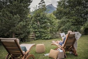 two chairs sitting in the grass with a person reading a book at Biohotel Rastbichlhof in Neustift im Stubaital