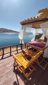 zwei Liegestühle und ein Sonnenschirm auf einer Terrasse neben dem Wasser in der Unterkunft Uros Utasa Lodge in Puno