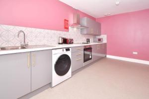 a pink kitchen with a washing machine and a sink at One Battison - Affordable Rooms, Suites & Studios in Stoke on Trent in Stoke on Trent