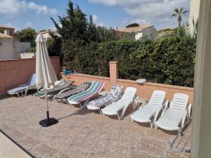 a group of lounge chairs and an umbrella on a patio at CHALET MUY CERCA DE LA PLAYA CON PISCINA PRIVADA in Orihuela Costa