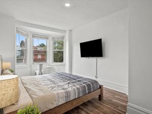 a white bedroom with a bed and a flat screen tv at Oakland/University @E Stylish and Central Private Bedroom with Shared Bathroom in Pittsburgh