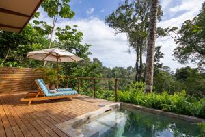 a deck with a chair and an umbrella next to a pool at El Remanso Rainforest Lodge in Puerto Jiménez