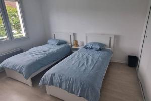 a bedroom with two beds with blue sheets and a window at Un Havre de Paix in Villepinte