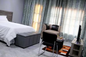 um quarto com uma cama, uma cadeira e uma televisão em De Ellas Boutique Lodge em Polokwane