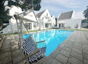 a swing in front of a house with a swimming pool at Adrift Guesthouse St Francis Bay in St Francis Bay