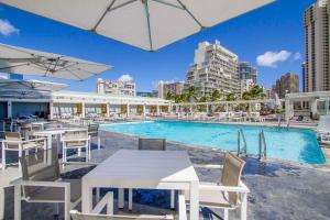 a pool with tables and chairs next to a building at Ocean Views from balcony Walk to Beach and Mall 3024 in Honolulu