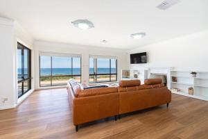 sala de estar con sofá marrón y ventanas en Beachfront Bliss- Aldinga Beach House - 5 BR, en Aldinga Beach