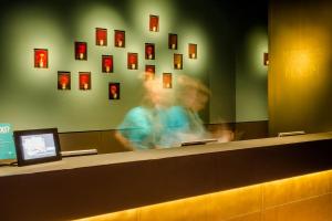 a woman is standing at a counter in a waiting room at Motel One München - Deutsches Museum in Munich