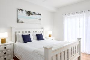 The Tides Beach House في خليج نيلسون: غرفة نوم بيضاء مع سرير أبيض مع وسائد زرقاء