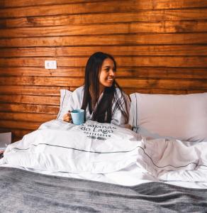 a woman sitting in bed with a cup of coffee at Hospedagem Cabanas do Lago Urubici in Urubici