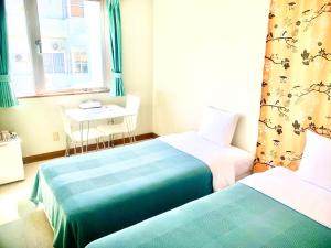 2 Betten in einem Zimmer mit einem Tisch und einem Fenster in der Unterkunft Hotel Happy Holiday Ishigaki in Ishigaki-jima