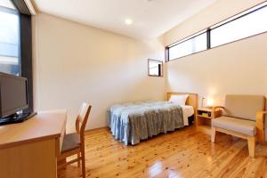 a bedroom with a bed and a desk and a tv at Yamashitako Lodge in Yufuin