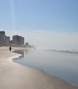 una persona caminando por la playa cerca del agua en Resort Itanhaém - Pé na areia, en Itanhaém