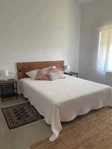 a white bedroom with a large white bed with pink pillows at El paller de L´Armentera 3 in Saldet
