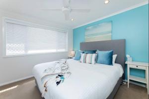 a bedroom with a white bed with blue walls and a window at Coral Sands 2 in Forster