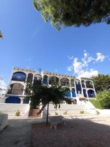 Un edificio con ventanas azules y un árbol al frente. en Apartamento, 3° línea de playa, en Cubelles