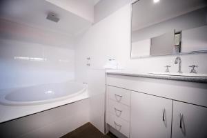 a white bathroom with a sink and a tub at Island Palms Motor Inn in Forster
