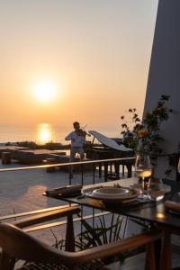 イアにあるSanto Pure Oia Suites & Villasの夕日を背景にテーブルに立つ女