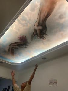 een kind reikt naar een schilderij op het plafond bij The juannas hostal y bistro cultural in Rivera