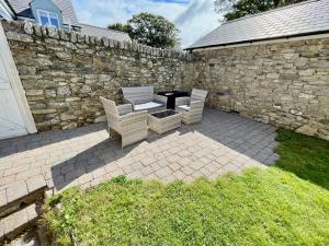 un patio con mesa, sillas y pared de piedra. en Cosy Cottage - Whitchurch, Solva en Solva