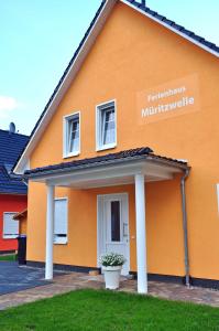 ein orangenes Haus mit einem Schild an der Seite in der Unterkunft Ferienwohnungen Appartements - Ferienhaus Müritzwelle in Marienfelde
