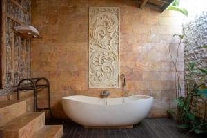a bath tub in a bathroom with a brick wall at Ubud Lestari Villa in Ubud