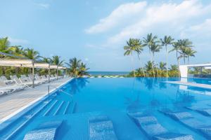 a swimming pool with palm trees and the ocean at Riu Sri Lanka All Inclusive in Bentota