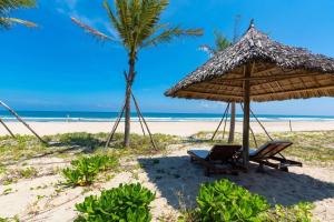 ダナンにあるOcean Beach Villas Danangの椰子の木と藁の傘と椅子が並ぶビーチ