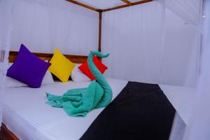 un dinosaurio de juguete verde sentado en una cama con almohadas coloridas en Sajana Ocean Hill, en Mirissa