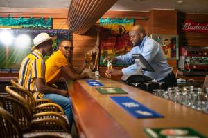 three men sitting at a bar in a restaurant at Piggs Peak Hotel in Piggs Peak