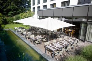 un restaurante con mesas y una sombrilla junto a una piscina en Fürstenfelder Hotel, en Fürstenfeldbruck