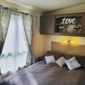 a bedroom with a large bed and a window with the words love at Kjs holiday home in Saint Osyth