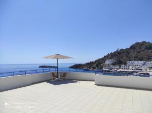 een patio met een parasol en stoelen en de oceaan bij Protopapas Rooms in Loutro