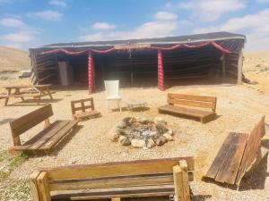 a hut with benches and a fire in the desert at חאן נחל חווה Han Nahal Hava in Mitzpe Ramon