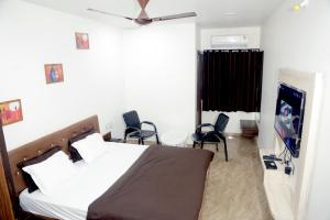 a bedroom with a bed with chairs and a flat screen tv at Hotel Kiwi Inn in Indore