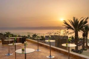 eine Hotelterrasse mit Tischen und Meerblick in der Unterkunft Hilton Dead Sea Resort & Spa in Sowayma