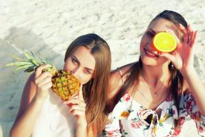 deux femmes sur la plage tenant un ananas et une orange dans l'établissement Hilton Dead Sea Resort & Spa, à Sowayma