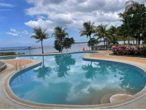 a swimming pool next to the beach with palm trees at Modern Unit Near The Beach at Canyon Cove Nasugbu in Nasugbu