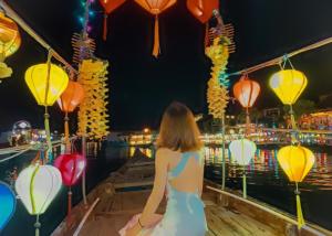 a woman is standing on a boat with lanterns at The House 36 in Hoi An