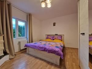 a bedroom with a bed with purple sheets and a window at Sabina's Cozy House in Buşteni