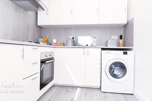 cocina con armarios blancos, lavadora y secadora en City Village en Bickley