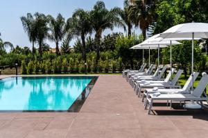 a row of lounge chairs with an umbrella next to a swimming pool at Virdamuri - Etna Country Resort in Giarre