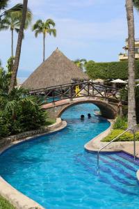 a swimming pool with a bridge and palm trees at Departamento Frente a la Playa, Velas Vallarta in Puerto Vallarta