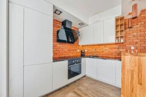 a kitchen with white cabinets and a brick wall at Golden Apartments Gdansk&SwB12 in Gdańsk