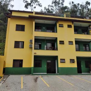 een geel gebouw met groene deuren op een parkeerplaats bij Flats e Apartamentos Temporada Mar Brasil in Ubatuba