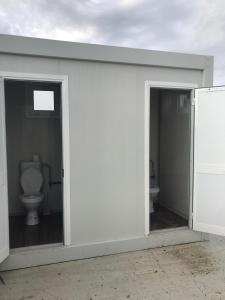 a white building with two doors and a toilet at Agri Camping italiano - Eucalyptus in Shënkoll