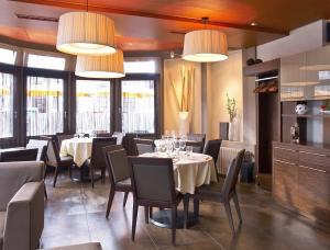 una sala da pranzo con tavoli, sedie e lampadari a braccio di Hôtel la Suite a Payerne