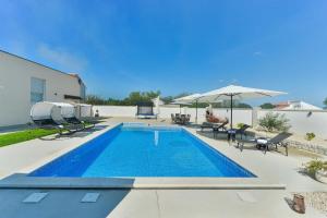 a swimming pool with chairs and an umbrella next to a house at Villa Miranda with pool in Zaton